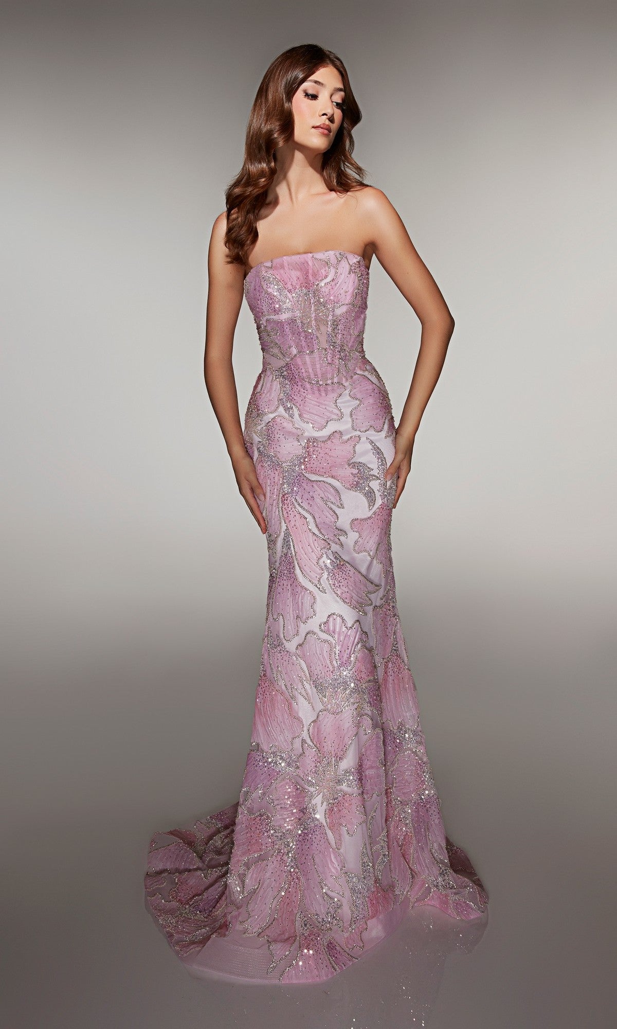 A woman in the Alyce 62049 long prom dress, featuring pink and white floral patterns, sequins, and a sheer corset bodice, stands against a plain neutral background.